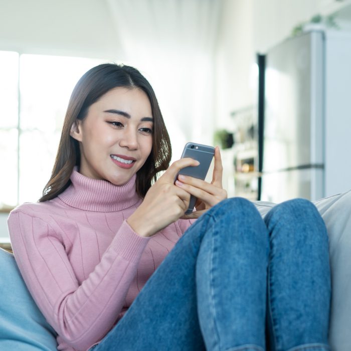 ASIAN BEAUTIFUL WOMAN SIT ON SOFA AND CHAT ON MOBILE PHONE IN HOUSE HAPPY ATTRACTIVE YOUNG GIRL SPEND LEISURE TIME AT HOME FEEL RELAX AND ENJOY COMMUNICATE AND DISCUSS ON SMARTPHONE IN LIVING ROOM